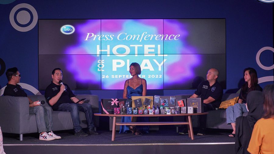 Speakers on stage at the Hotel for Play press conference in front of a pink and purple screen