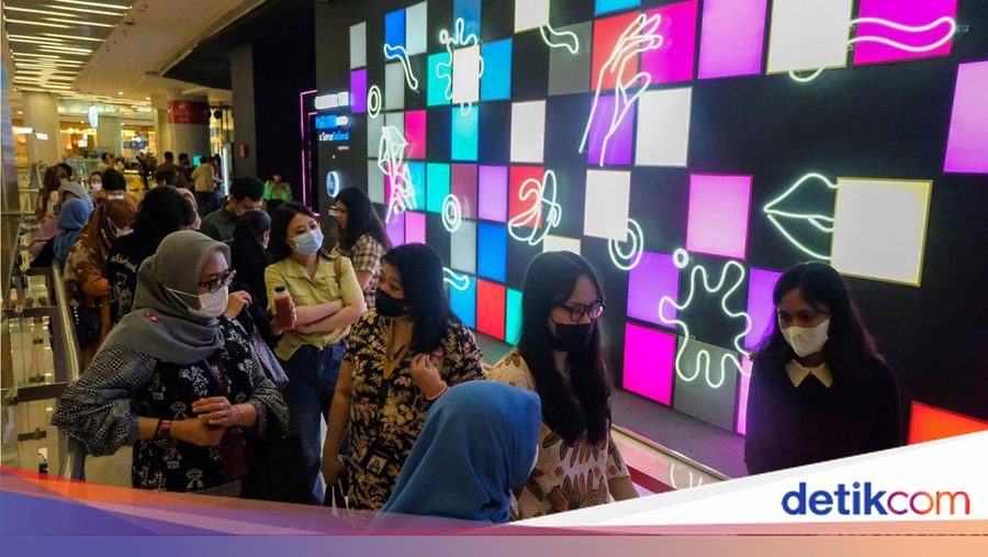 Masked visitors walking past a neon-lit wall of pink and blue tiles at Hotel for Play