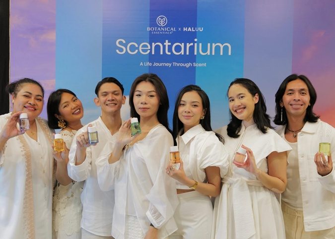Eight people in white holding perfume bottles in front of the Scentarium launch backdrop